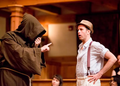 Duke hooded face totally covered in hood of his monk's habit, gestures with a pointed finger as Lucio, hands on hips, wearing whit work shirt and white pants, with suspenders and fedora, looks in astonishment.
