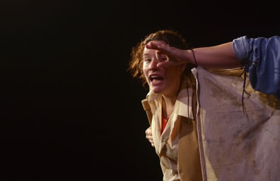 On a dark background, Bottom in rustic vest peers through Wall's finger's forming a circle