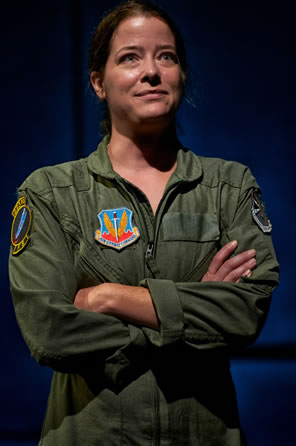 The Pilot in olive green flight suit, with a unit patch on the right breast. stands with arms crossed, looking confidently to the horizon