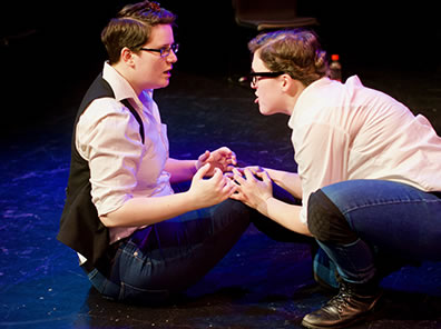 Production of Nicola Collett sits on ground wearing a black vest, Hannah Sweet opposite in black frame glasses